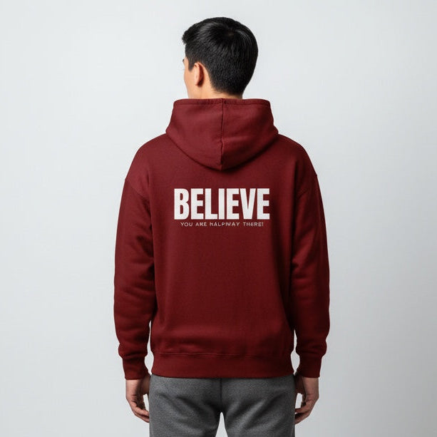 Person wearing a maroon hoodie with 'BELIEVE' text on the back against a white background