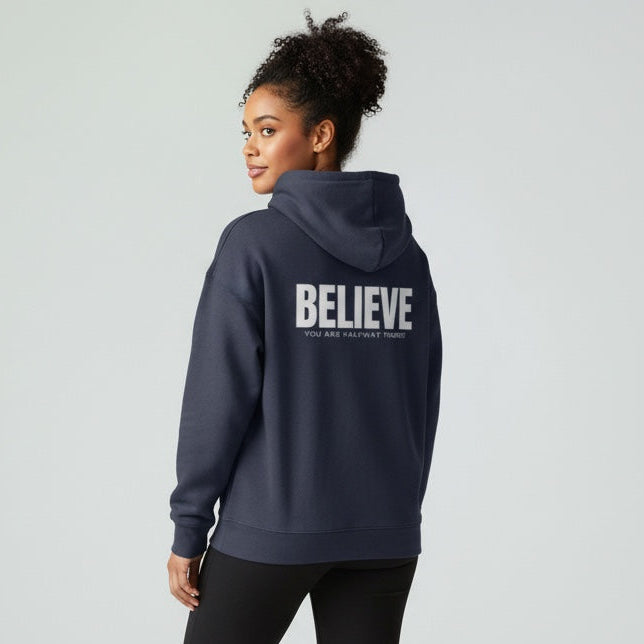 Person wearing a navy hoodie with 'BELIEVE' printed on the back, standing against a light gray background.