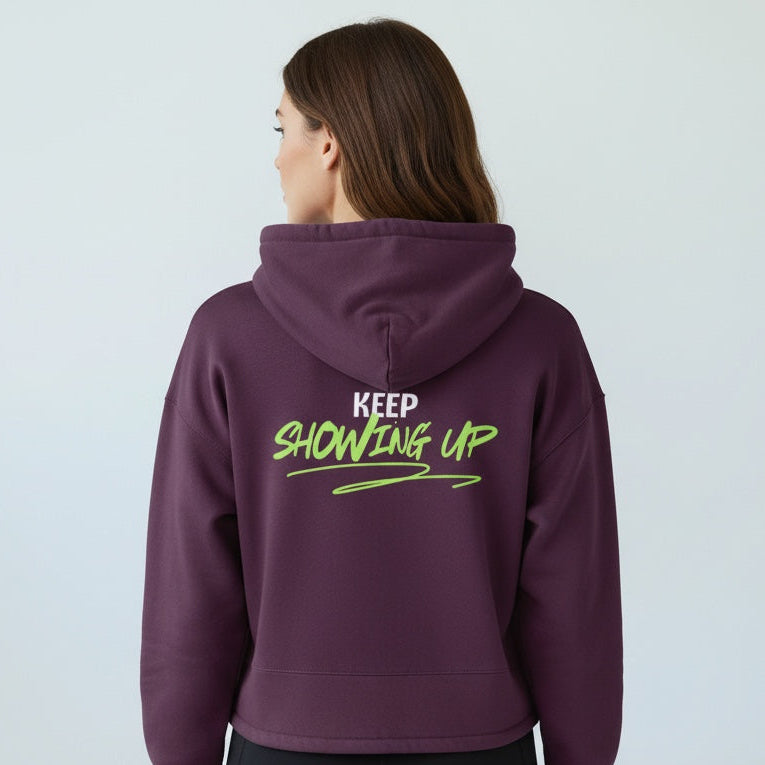 Person wearing a purple hoodie with 'KEEP SHOWING UP' text on the back against a light gray background