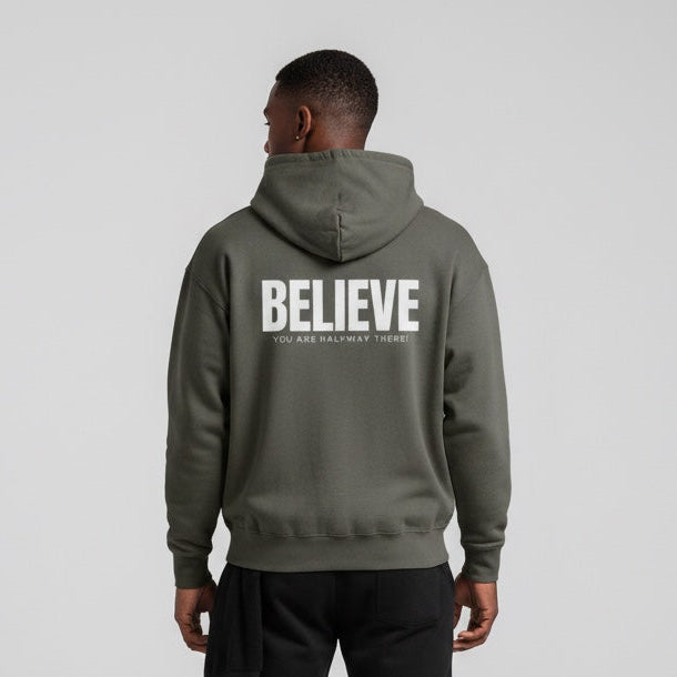 Person wearing a gray hoodie with 'BELIEVE' printed on the back, standing against a light gray background.